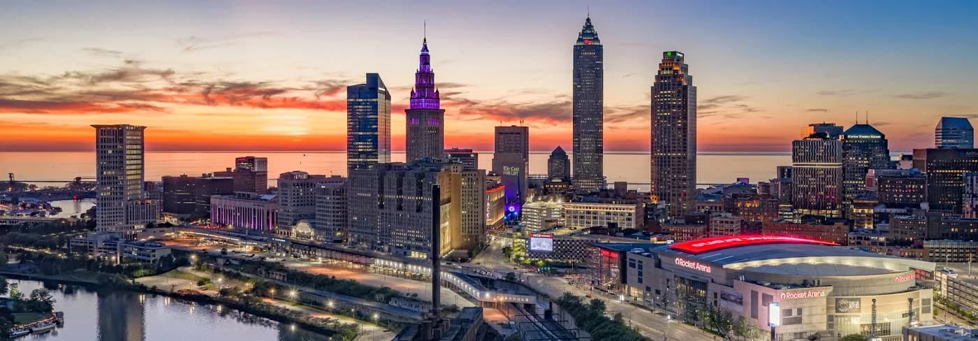 Wide aerial panorama of the Cleveland skyline and Cuyahoga River at sunset.